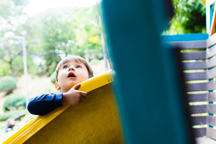 foto colorida. uma criança olha para o céu enquanto segura no brinquedo do parque. 