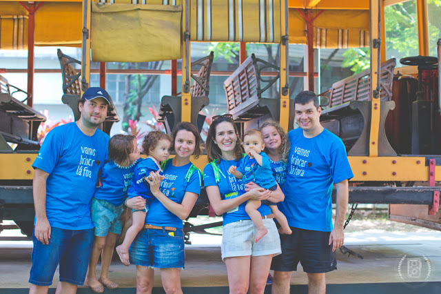 duas famílias com crianças pequenas vestindo a camiseta vamos brincar lá fora. o registro é em um museu.