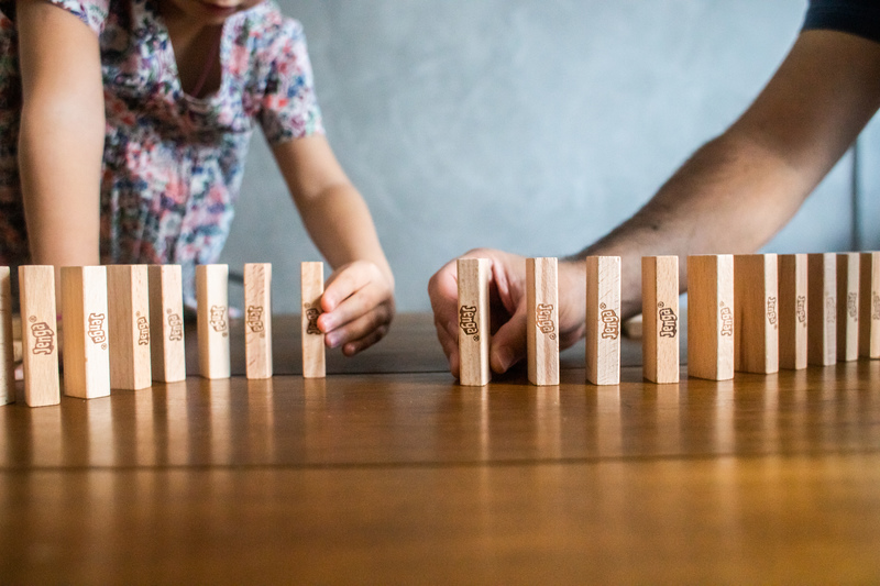 Um adulto e uma criança empilham blocos de madeira sob uma mesa construindo uma sequência