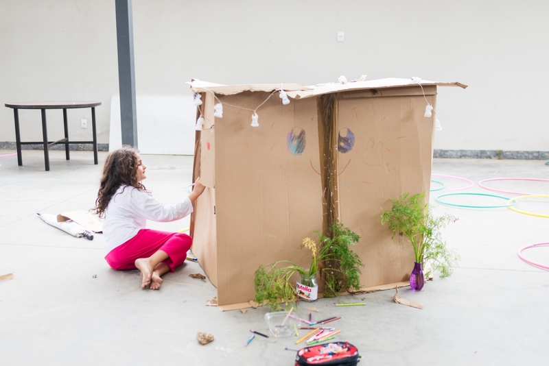 Uma menina decora uma casinha feita com caixa de papelão