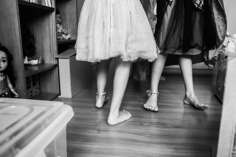 Duas meninas brincam em uma sala vestidas com saias de tule. O corte da imagem é na altura dos joelhos.