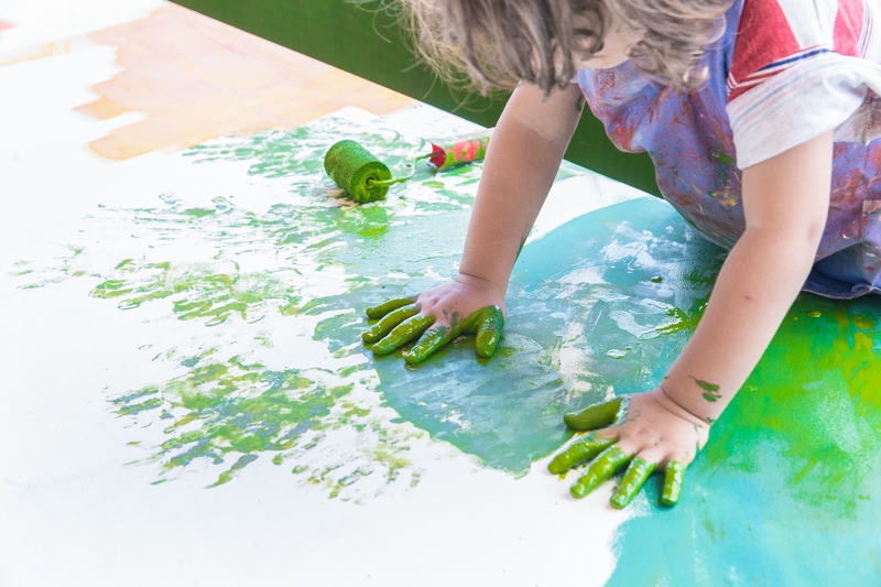 Foto de uma criança brincando com tinta verde. A imagem mostra as mãos pintadas.
