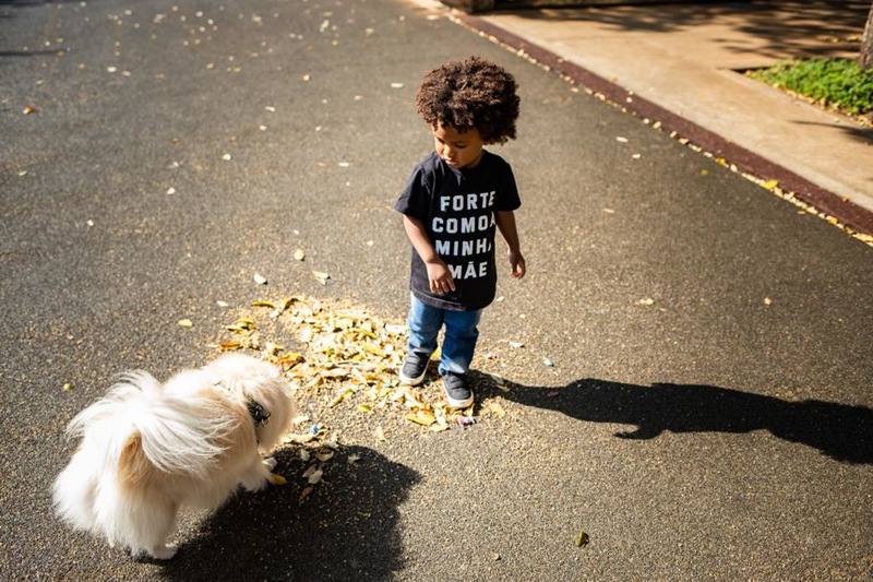 Foto de uma criança negra observando um cachorro em uma praça 