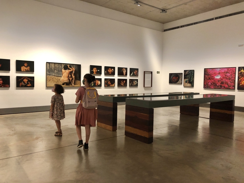 Foto de duas meninas observando as fotografias dos indígenas dentro da galeria
