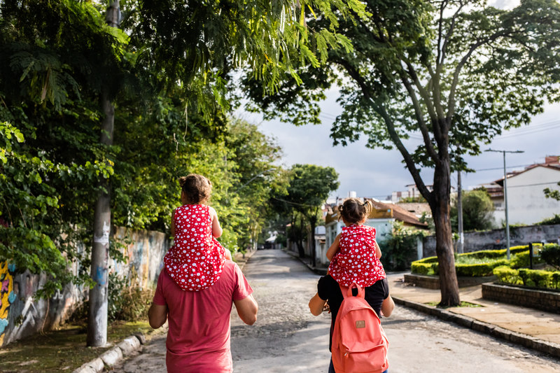 Em uma rua do bairro santa tereza em belo horizonte, um casal caminha com as crianças em seus ombros.