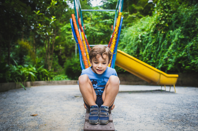 Foto colorida. Uma criança brinca na escada de um brinquedo em um parque. 