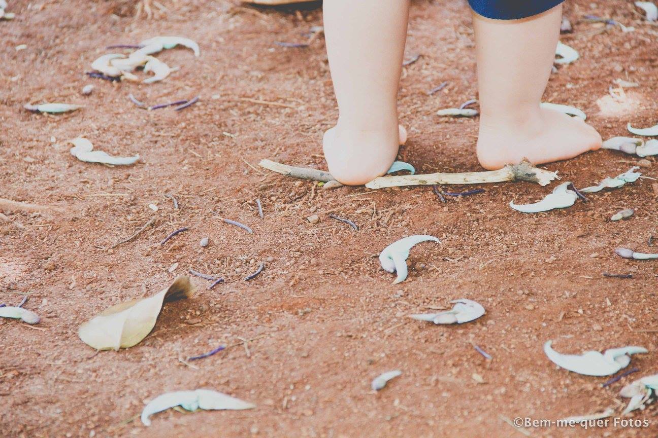 foto colorida. em um chão de terra batida, os pés de uma criança caminhando. 