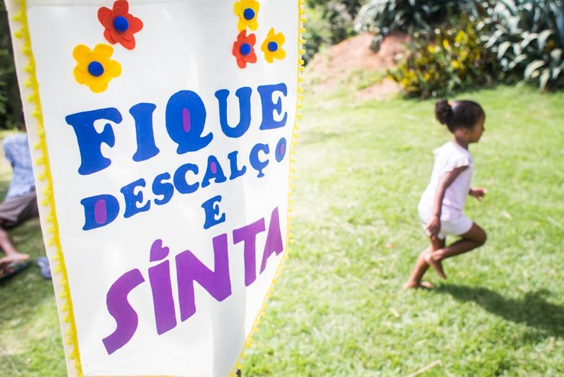 foto colorida. uma criança corre descalça pela grama. em primeiro plano, um estandarte escrito "fique descalço e sinta"