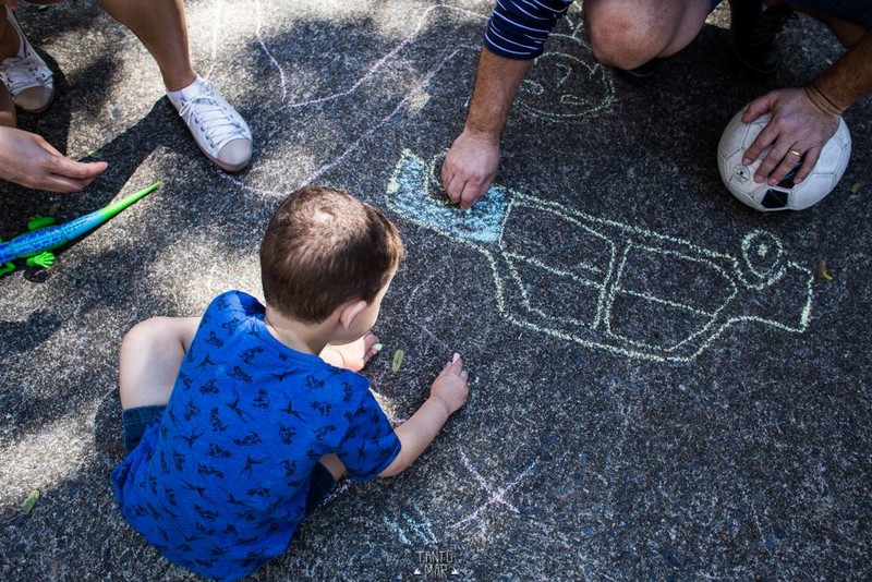 foto colorida. uma criança e um adulto desenham com giz no chão da praça.