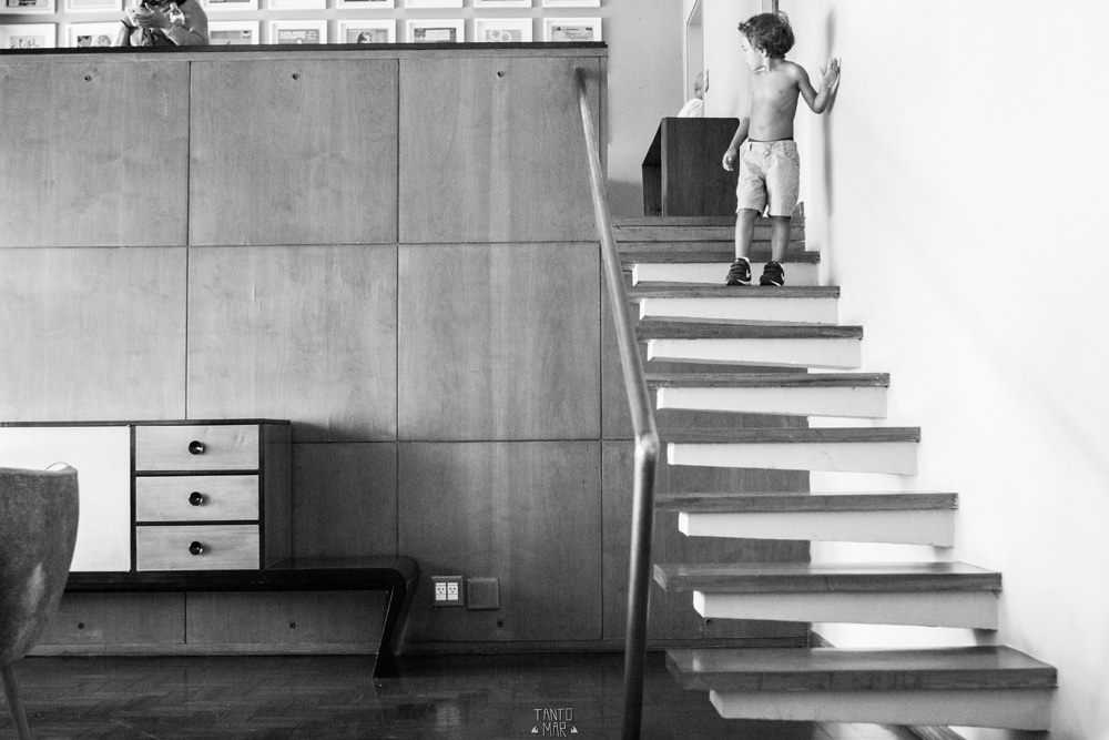 foto preto e branco. uma criança desce a escada da sala da casa.