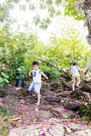 foto colorida. duas crianças andam sob pedras no jardim.
