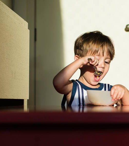 foto colorida. uma criança coloca uma colher na boca enquanto segura um bowl.