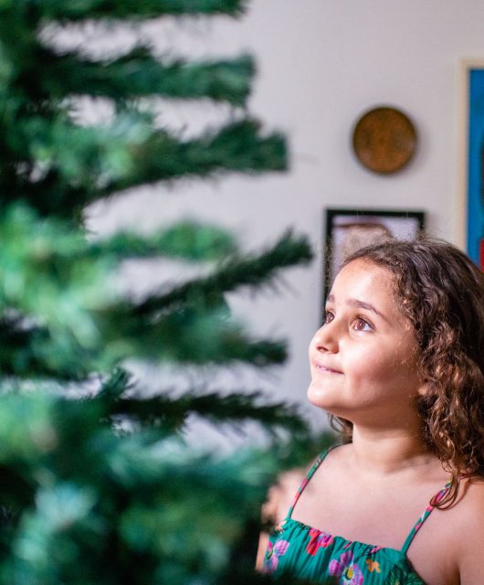 foto colorida. uma criança observa uma árvore de natal na sala de casa.
