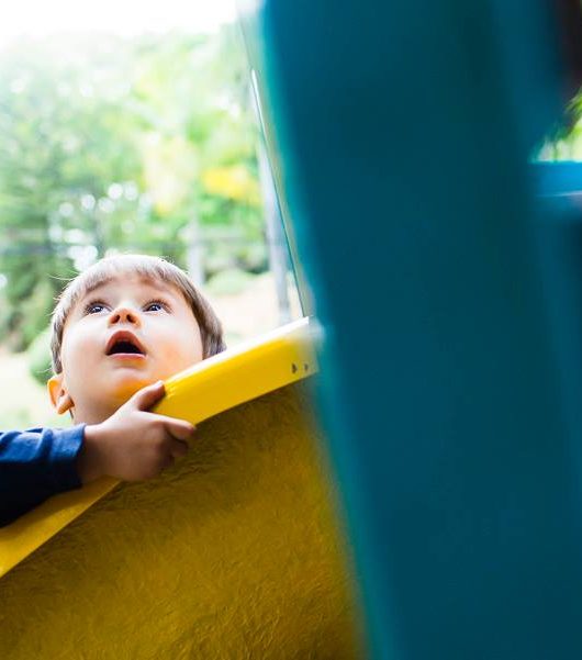 foto colorida. uma criança olha para o céu enquanto segura no brinquedo do parque.