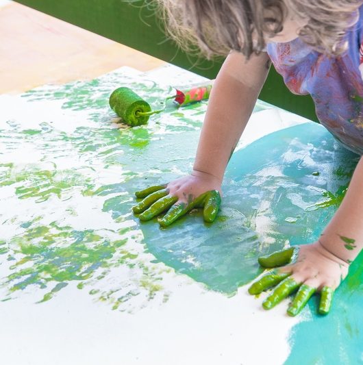Foto de uma criança brincando com tinta verde. A imagem mostra as mãos pintadas.