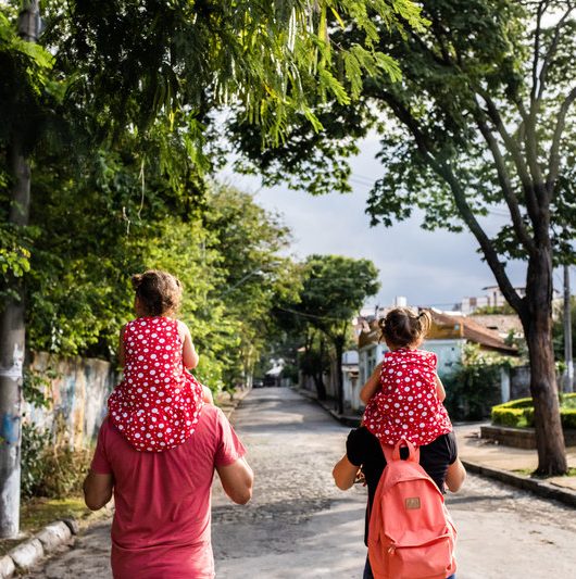 Em uma rua do bairro santa tereza em belo horizonte, um casal caminha com as crianças em seus ombros.