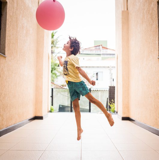 foto colorida. uma criança salta em direção a um balão vermelho.