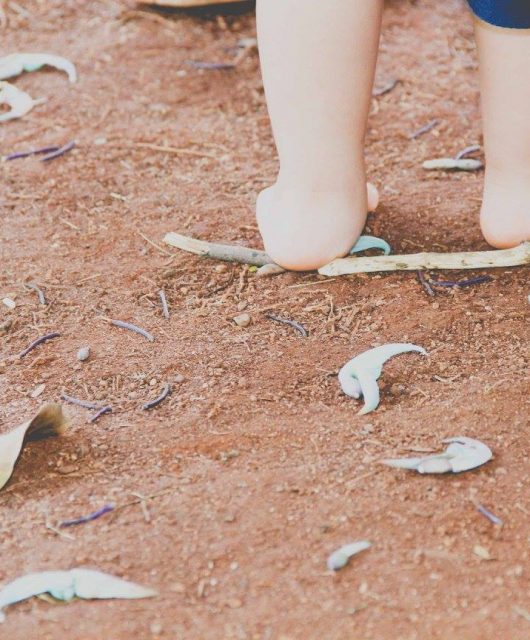foto colorida. em um chão de terra batida, os pés de uma criança caminhando.