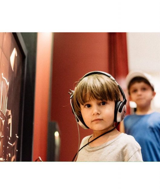 foto colorida. uma criança com fones de ouvido em uma exposição, olha para o espectador.